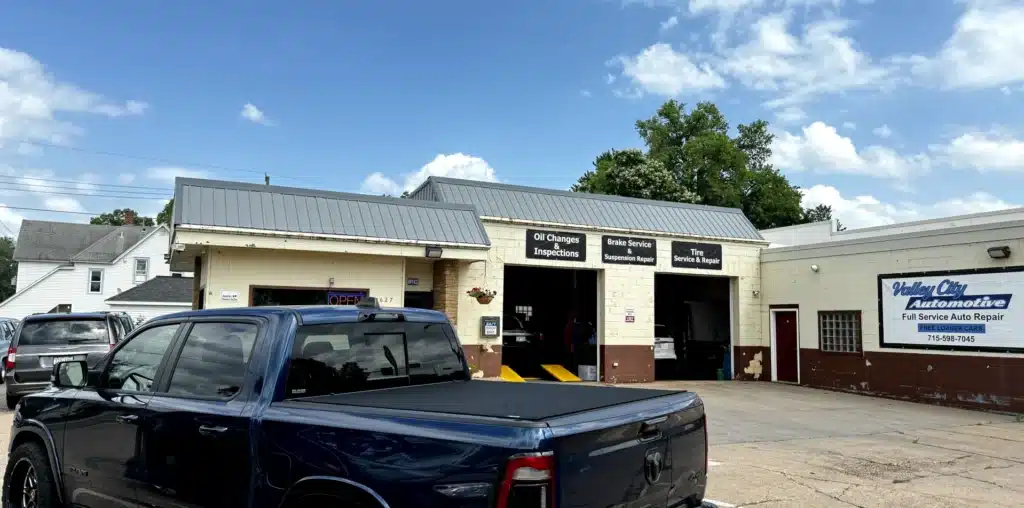 Auto repair in Eau Claire, WI, Valley City Automotive. A blue pickup truck is parked in front of "Valley City Automotive Full Service Auto Repair," a shop renowned for its auto repair services, including oil changes, inspections, brake services, and tire services. The sky above Eau Claire is clear with some white clouds.