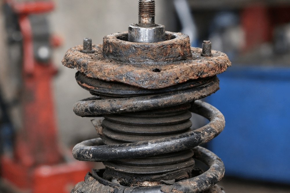 Close-up of a worn and corroded suspension strut assembly with the coil spring and upper mount visible before replacement.