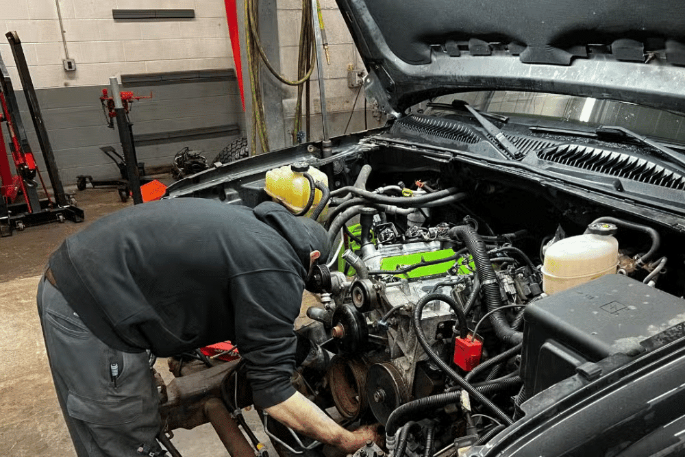 Valley City Automotive technician working inside a vehicle's engine compartment with the hood raised during engine service.
